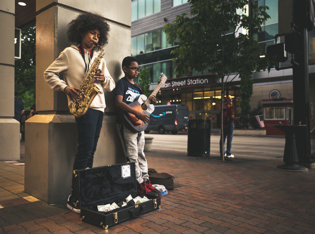 Two young musicians perform on a street for tips.
