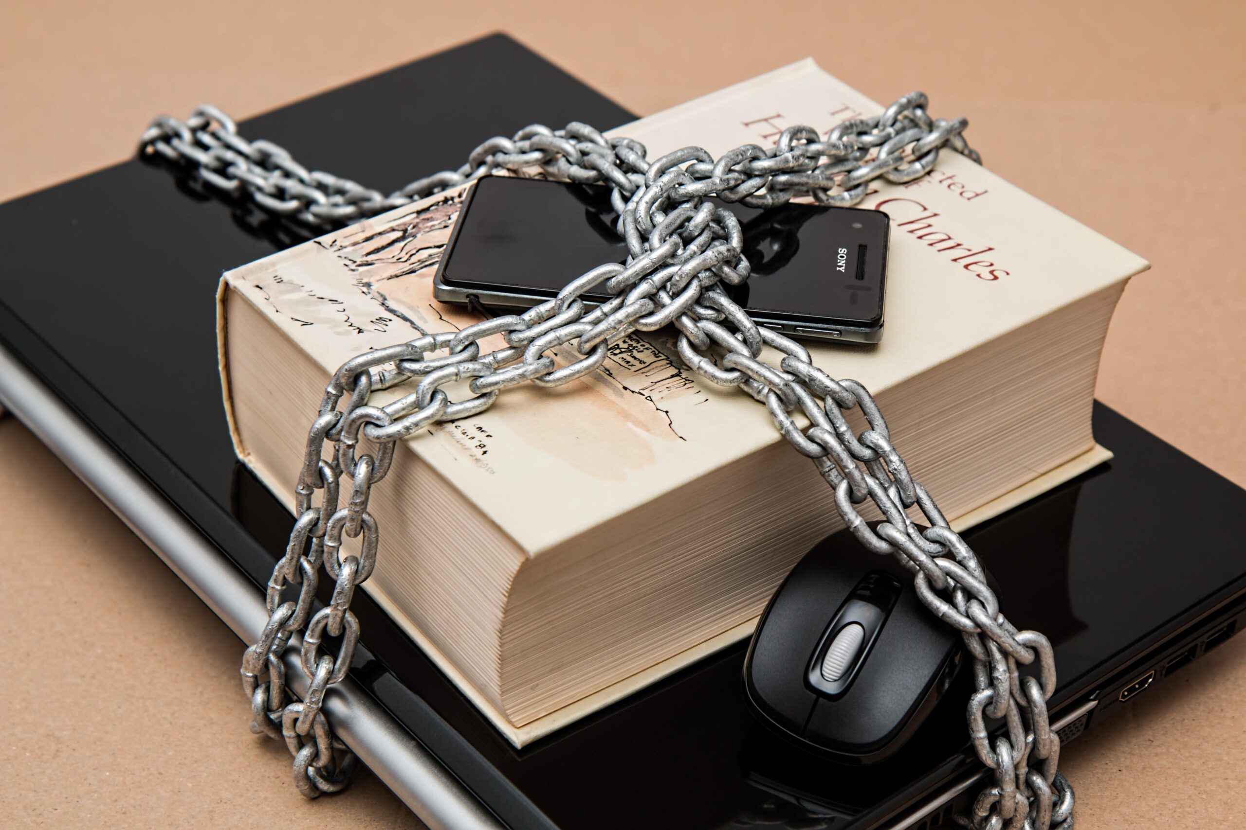 A computer, computer mouse, book, and phone are secured by a large chain.